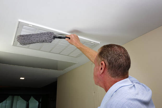 In Greenwich, CT, a worker dusts a ceiling intake HVAC furnace vent with a gray duster.