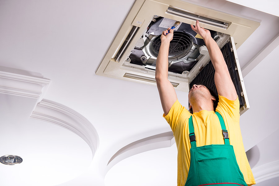 In Greenwich, CT, a young repairman is working on a ceiling air conditioning unit.