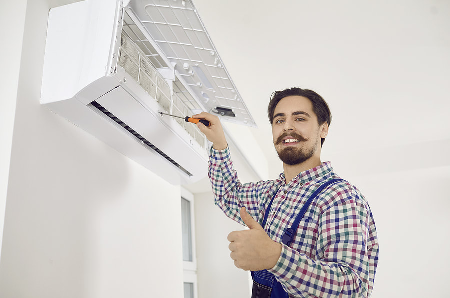 A happy AC repair worker shows thumbs up after fixing a wall air conditioner in Greenwich, CT.